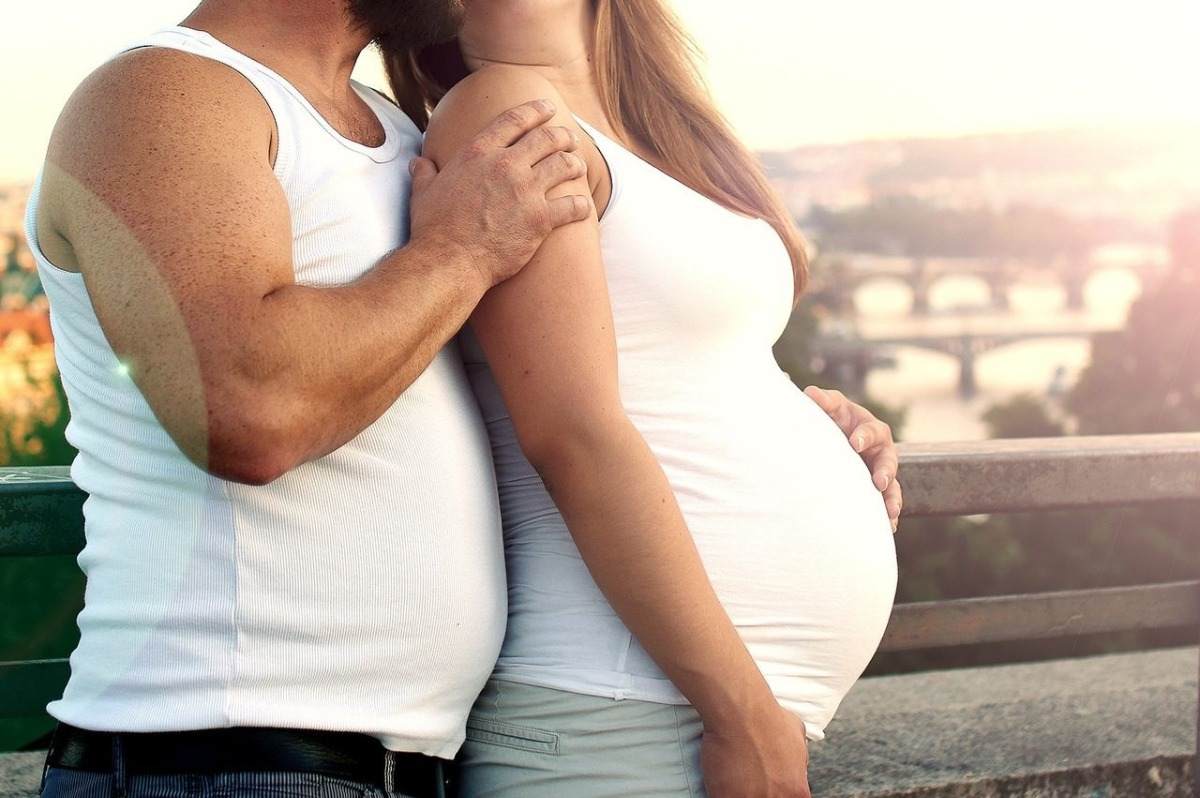 futuro pai com barriga de cerveja abraça a esposa ao pôr do sol