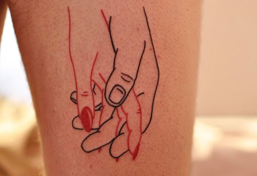 Ideia de tatuagem com as mãos de um casal de namorados em vermelho e preto na coxa