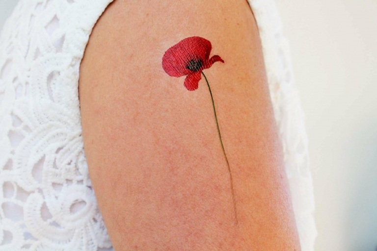 Tatuagem de senhora bonita com flor de papoula vermelha e haste verde sutil